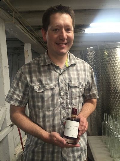 Dan Brown in the former dairy barn, now Deerfoot Winery, holding a bottle of his cherry wine.