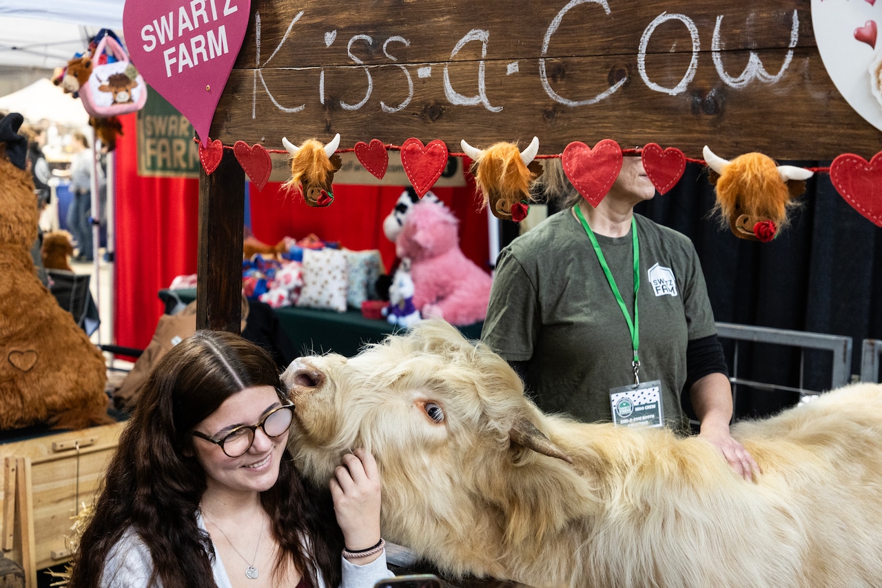 Visitors and a costumed cow at the Swartz Farm 'Kiss-a-Cow' booth on opening day of the 2026 Pa. State Farm Show.