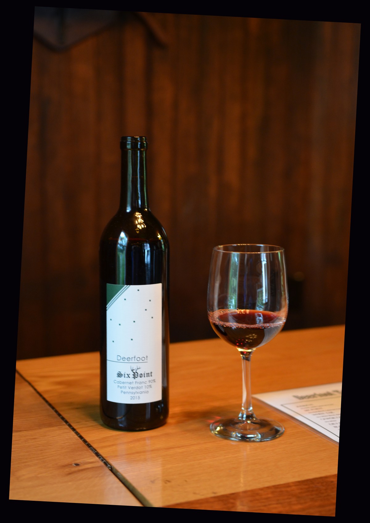 A bottle of Deerfoot Six Point Cabernet Franc with a glass of red wine on the tasting room bar.