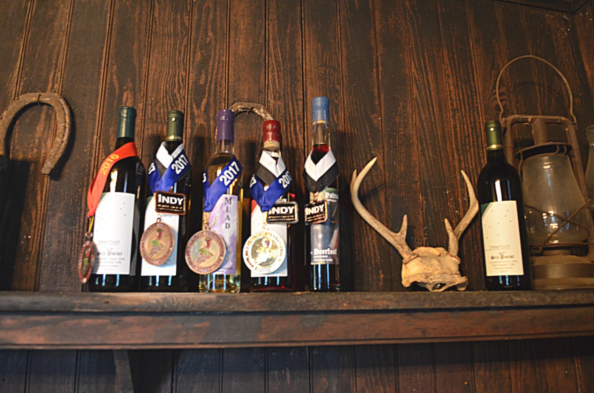 Award-winning Deerfoot wine bottles displayed on a shelf with medals from 2016 and 2017 competitions.