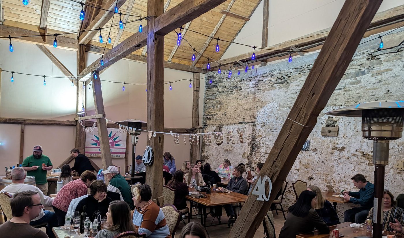 Guests gathered at long tables inside the Hay Loft at Deerfoot, with string lights overhead.